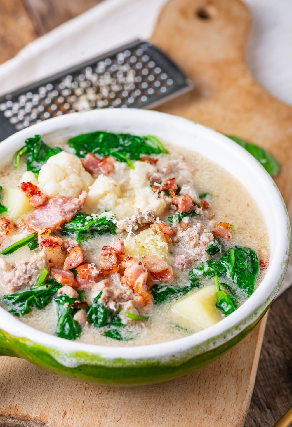 A green bowl with soup inside of it. The soup is topped with bacon bits and freshly grated white cheese.