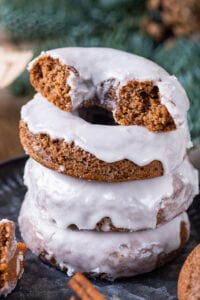 A stack of four glazed gingerbread donuts on a plate. The donut at the top of the stack is cut in half.