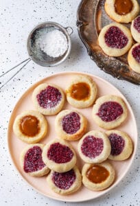 Thumbprint cookies on a nude colored plate set on a white speckled table.