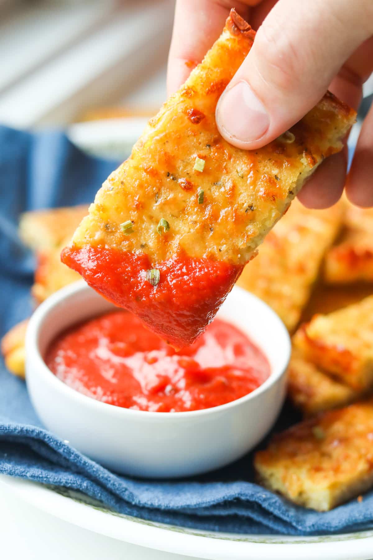 A hand holding a piece of cheese bread that's been dipped in marinara sauce.