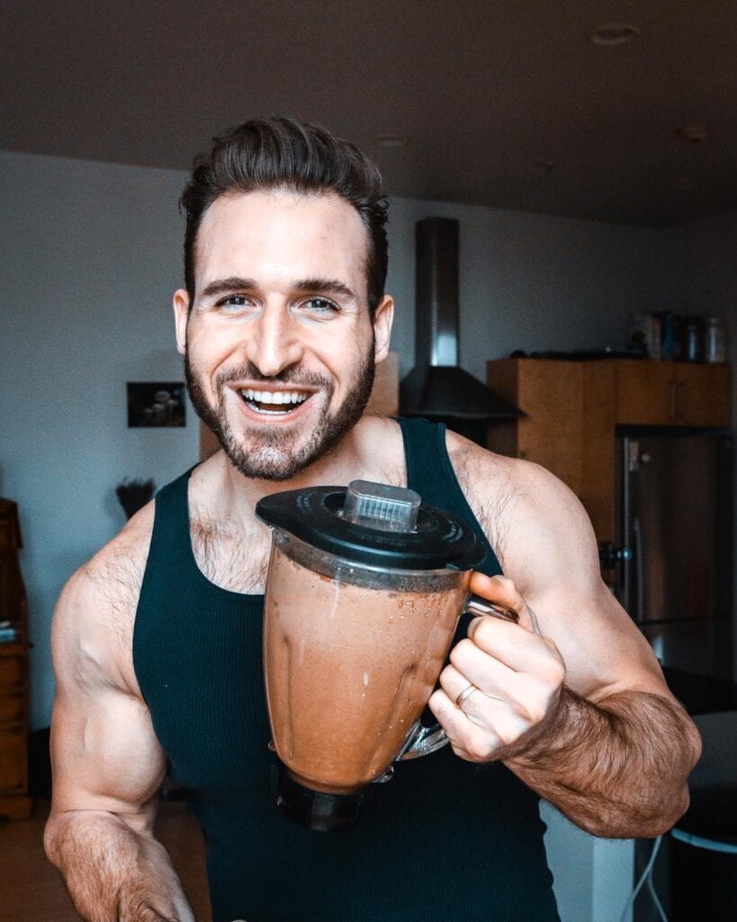 A guy in a black a-shirt holding a blender filled with chocolate protein.