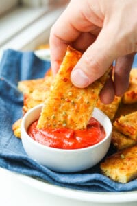 A hand dipping a slice of cheese bread into a cup of marinara.