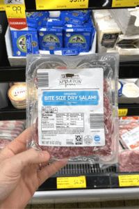 A hand holding a package of bite sized salami.