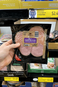 A hand holding a package of Canadian bacon.