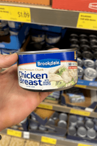 A hand holding a can of chicken breast meat.
