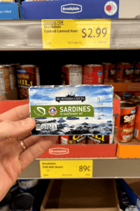 A hand holding a package of sardines.