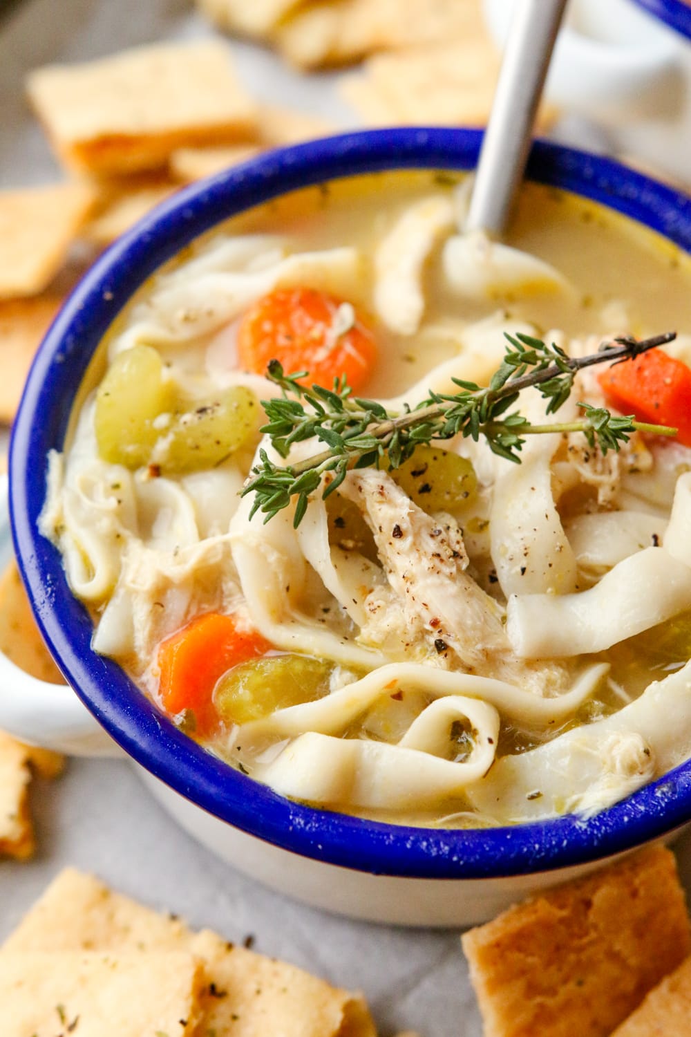 Chicken noodle soup in a white bowl with a blue rim. There is a spoon in the bowl.