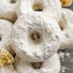 A donut set on top of other donuts. All of the donuts are covered in powdered sugar.