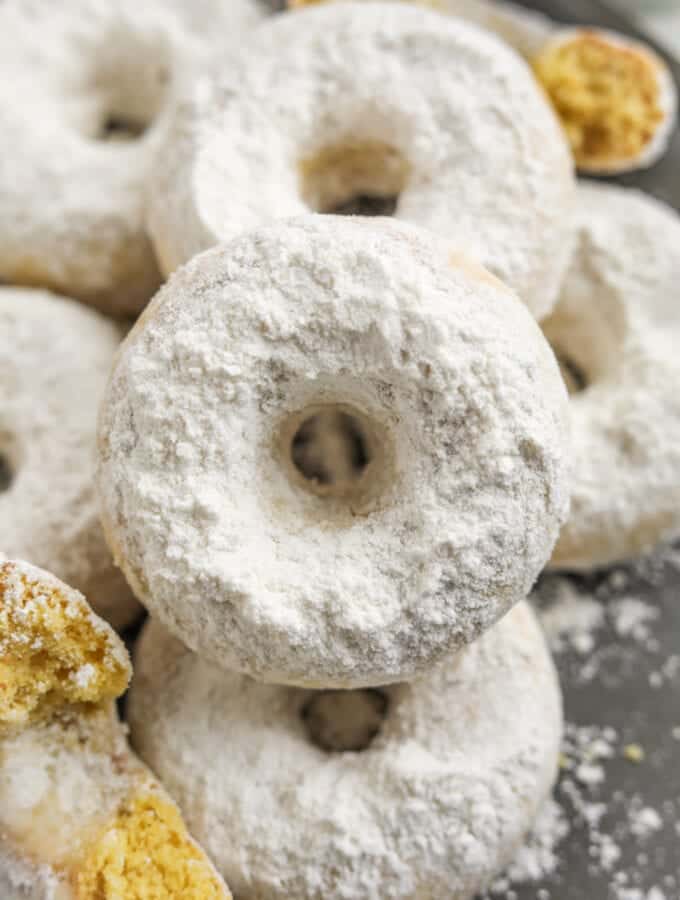 A donut set on top of other donuts. All of the donuts are covered in powdered sugar.