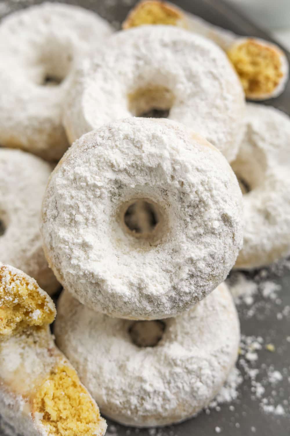 A donut set on top of other donuts. All of the donuts are covered in powdered sugar.