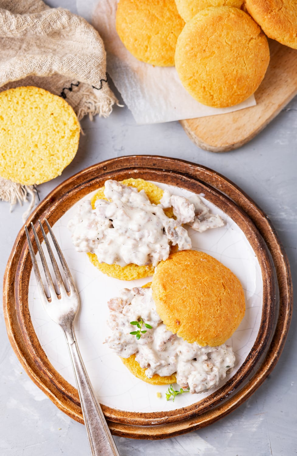 A plate with a biscuits and gravy on it. There are more biscuits scattered around the plate as well.