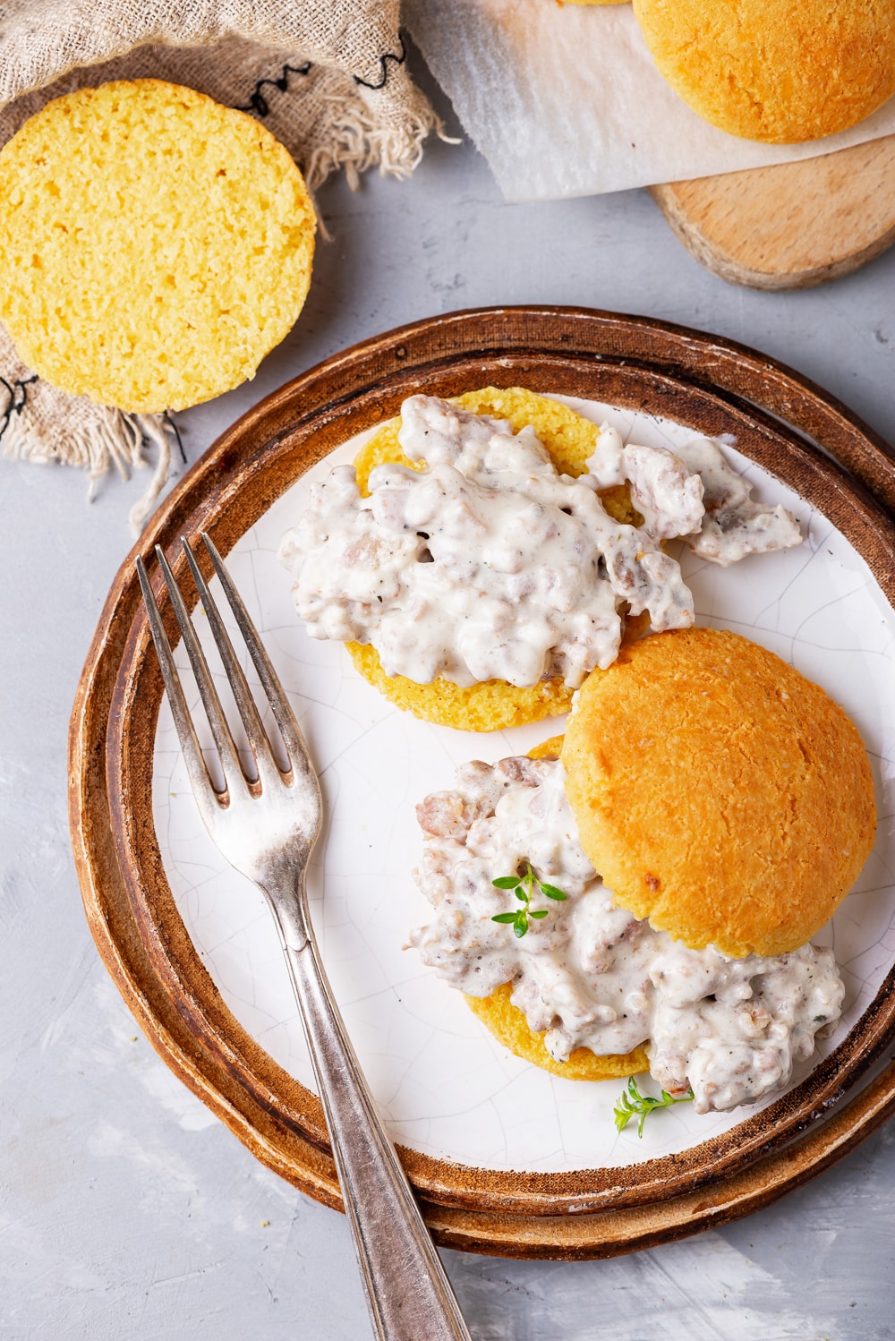 Biscuits covered in gravy on a plate. There is a fork on the plate, and more biscuits are by the plate as well.