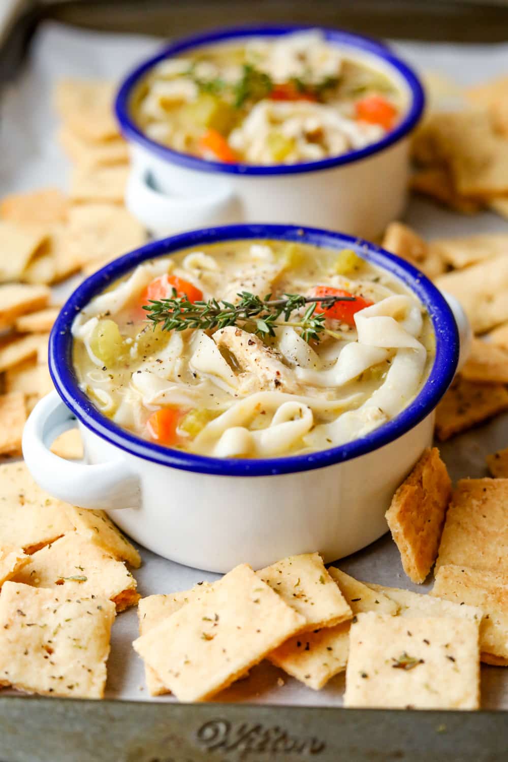 A bowl of chicken noodle soup on a baking sheet that's lined with parchment paper, and covered in crackers.