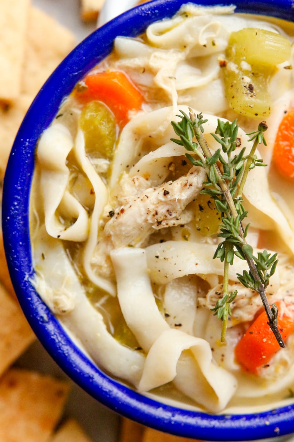 Chicken noodle soup in a bowl with a blue rim.