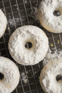 Powdered sugar donuts set on a wire rack. The rack is set on top of a baking sheet.
