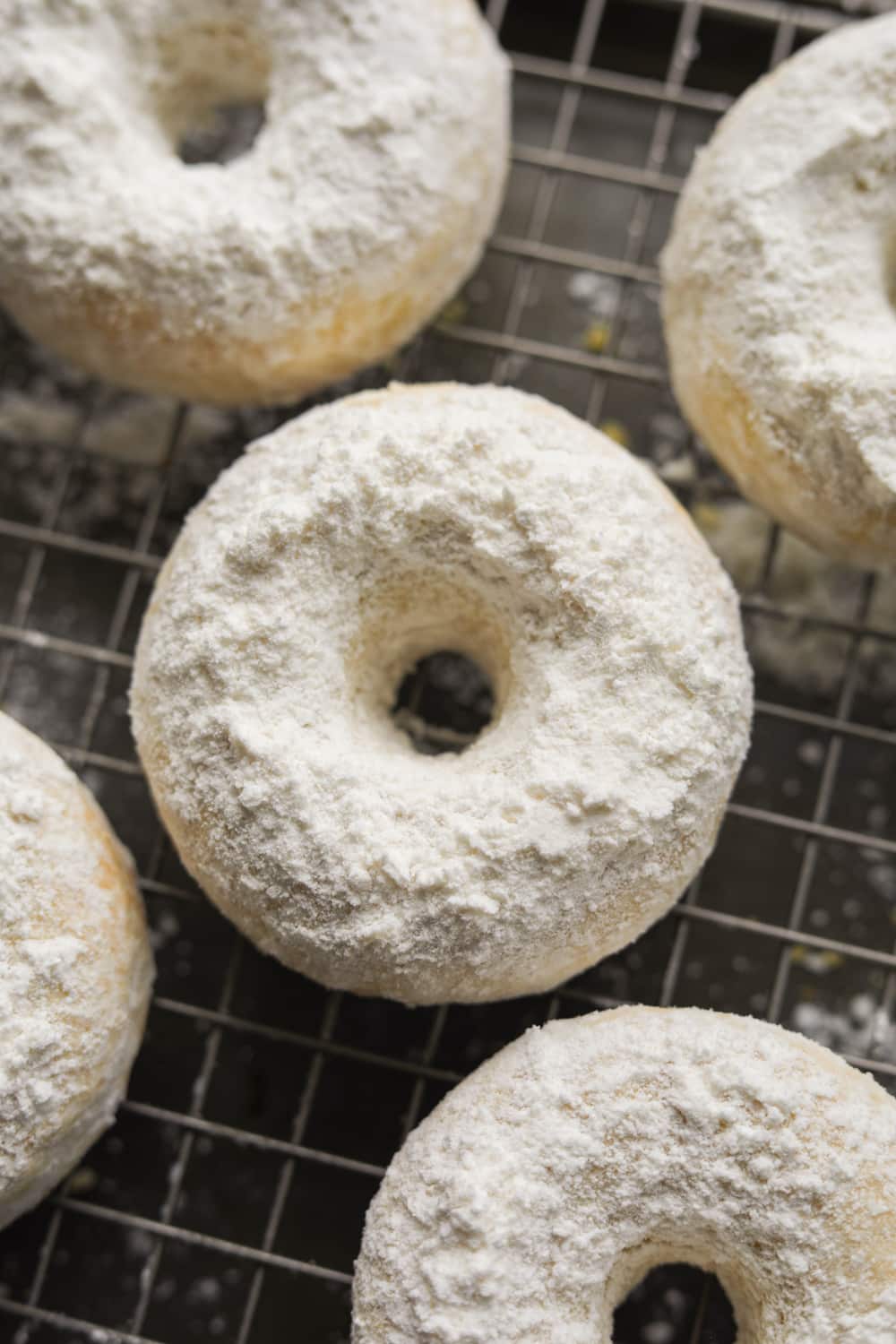 A powdered sugar donut on wire rack with other donuts around it.