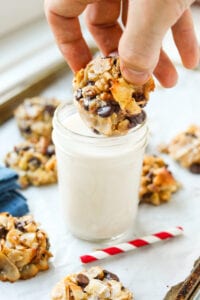 A hand removing a cookie from a glass of milk.