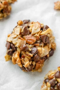 A cookie that has pieces of coconut, pecans, and chocolate chips in it.