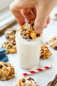 A hand dipping a cookie into a cup of milk.