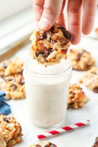 A hand holding a cookie above a glass of milk.