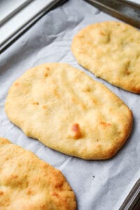 3 Pieces of naan bread on a baking sheet.