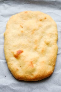 A plain naan bread on a white sheet of parchment paper.