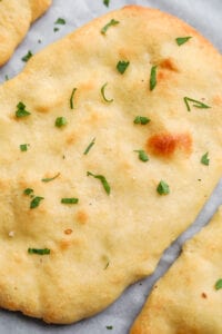 A piece of naan bread with chopped parsley on top of it.