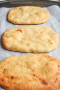 3 Naan breads laying on a baking sheet lined with parchment paper.