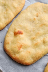 A piece of naan bread on a white sheet of parchment paper.