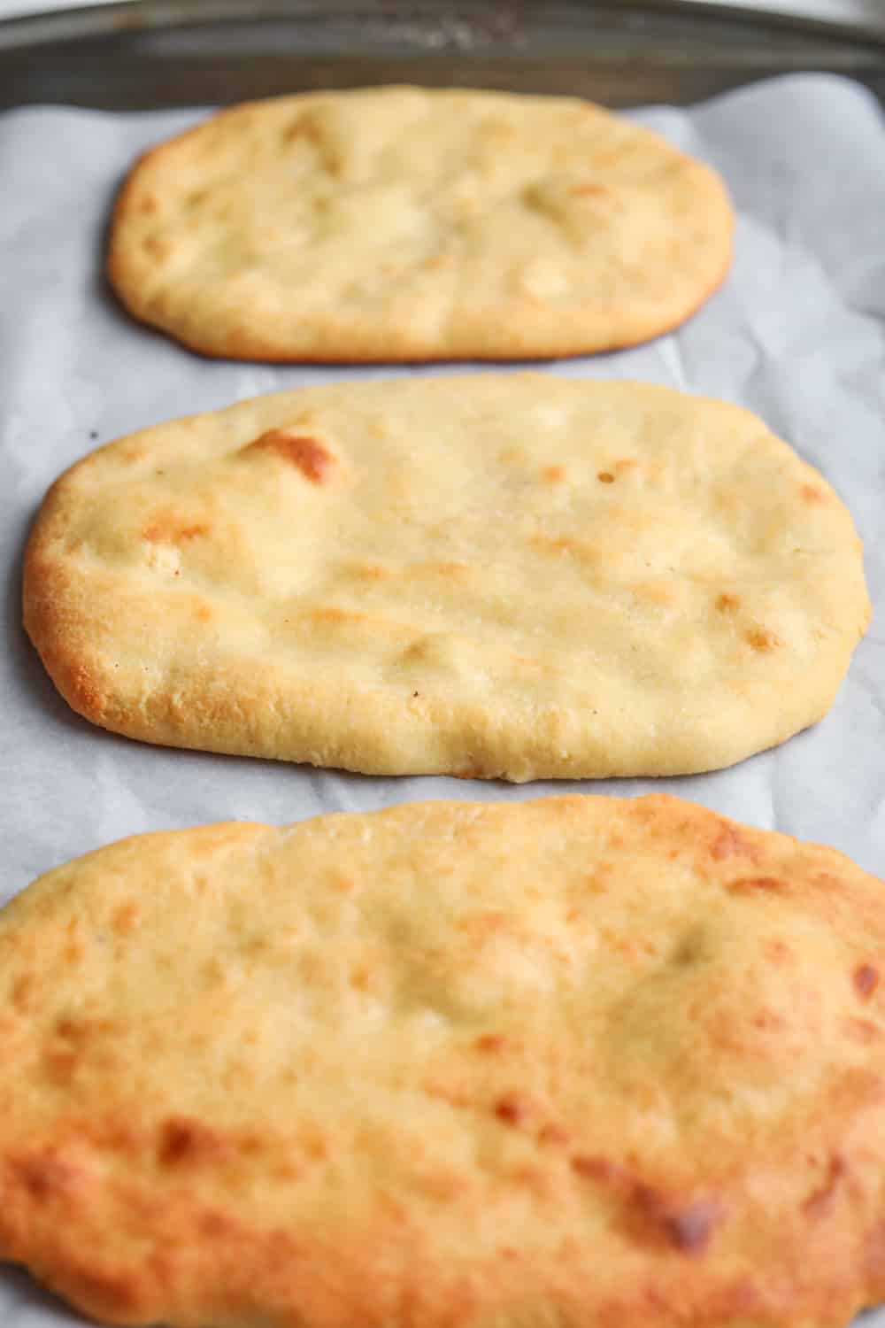 3 Naan breads laying on a baking sheet lined with parchment paper.