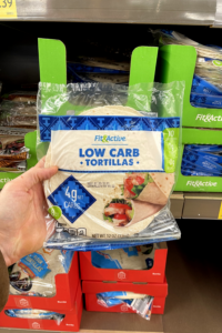 A hand holding a package of low carb tortillas.
