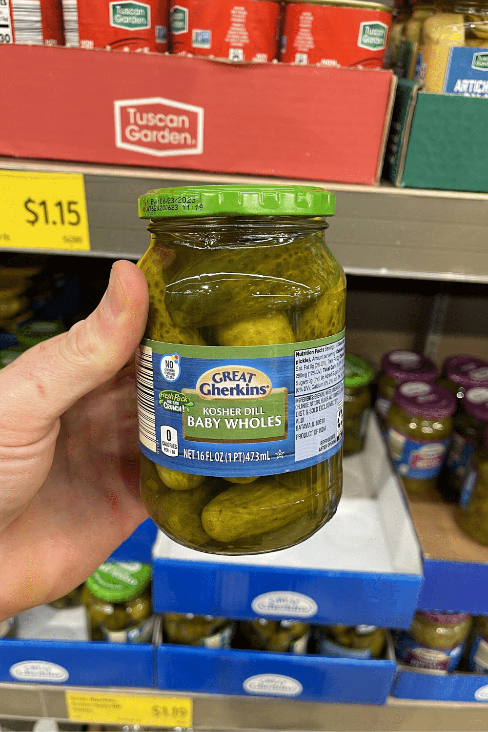 A hand holding a jar of baby dill pickles.