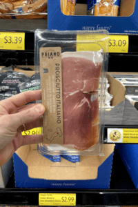 A hand holding a package of prosciutto.