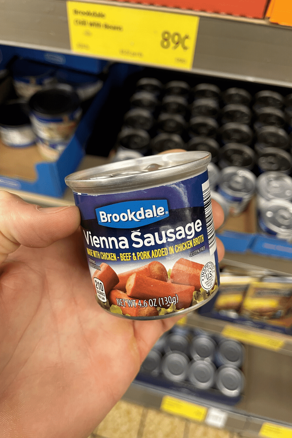 A hand holding a can of vienna sausages.