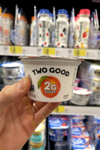 A hand holding a container of low sugar peach yogurt.