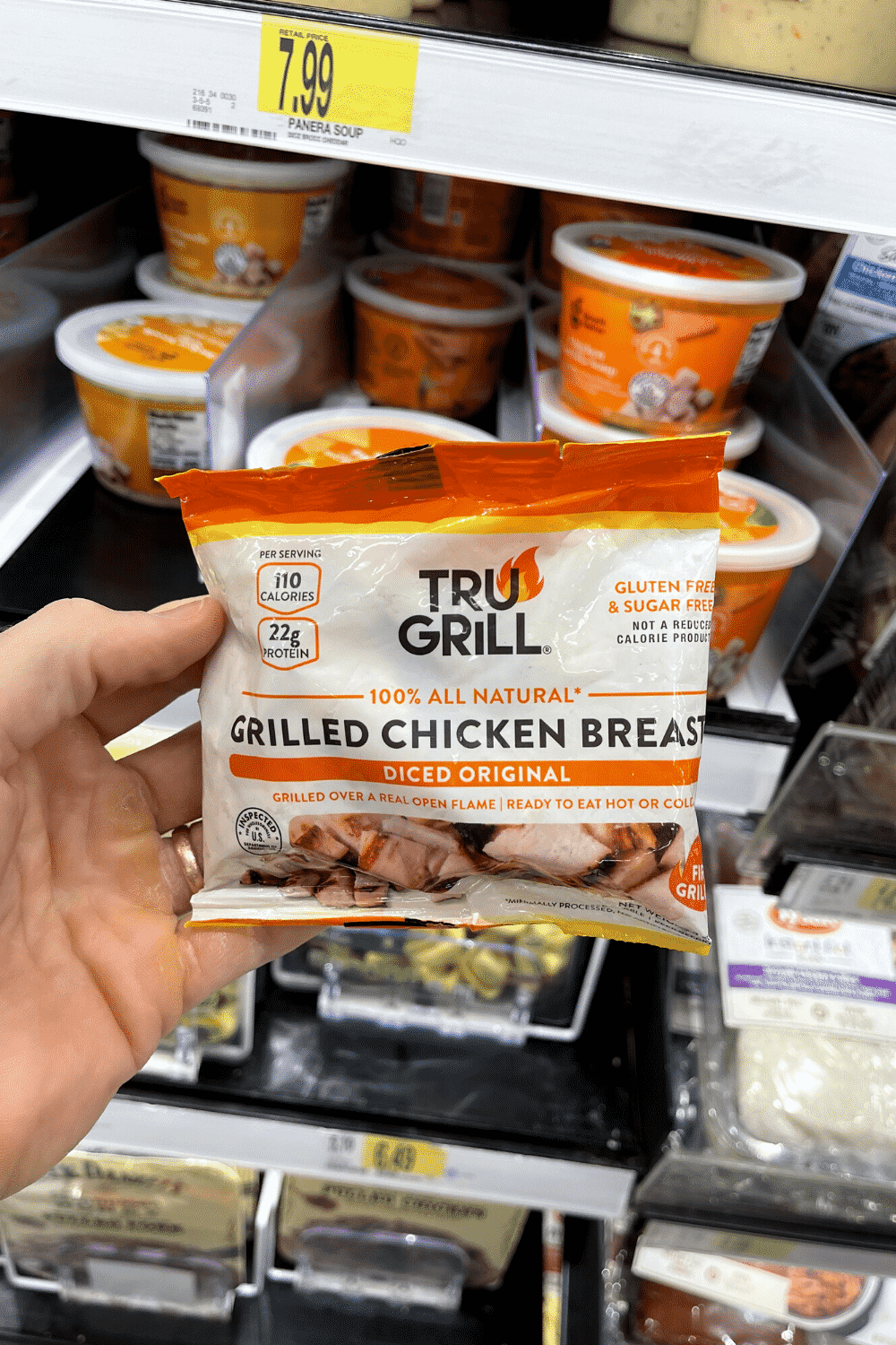 A hand holding a package of diced grilled chicken breast.