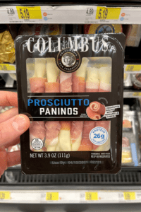 A hand holding a package of prosciutto paninos.
