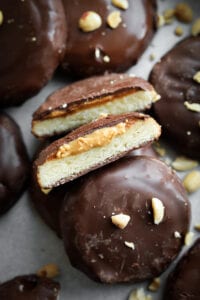 A chocolate covered cookie that's been cut in half and is set in between other chocolate cookies on a baking sheet lined with parchment paper.