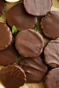 Chocolate covered cookies On a piece of brown parchment paper with mint leaves next to them.