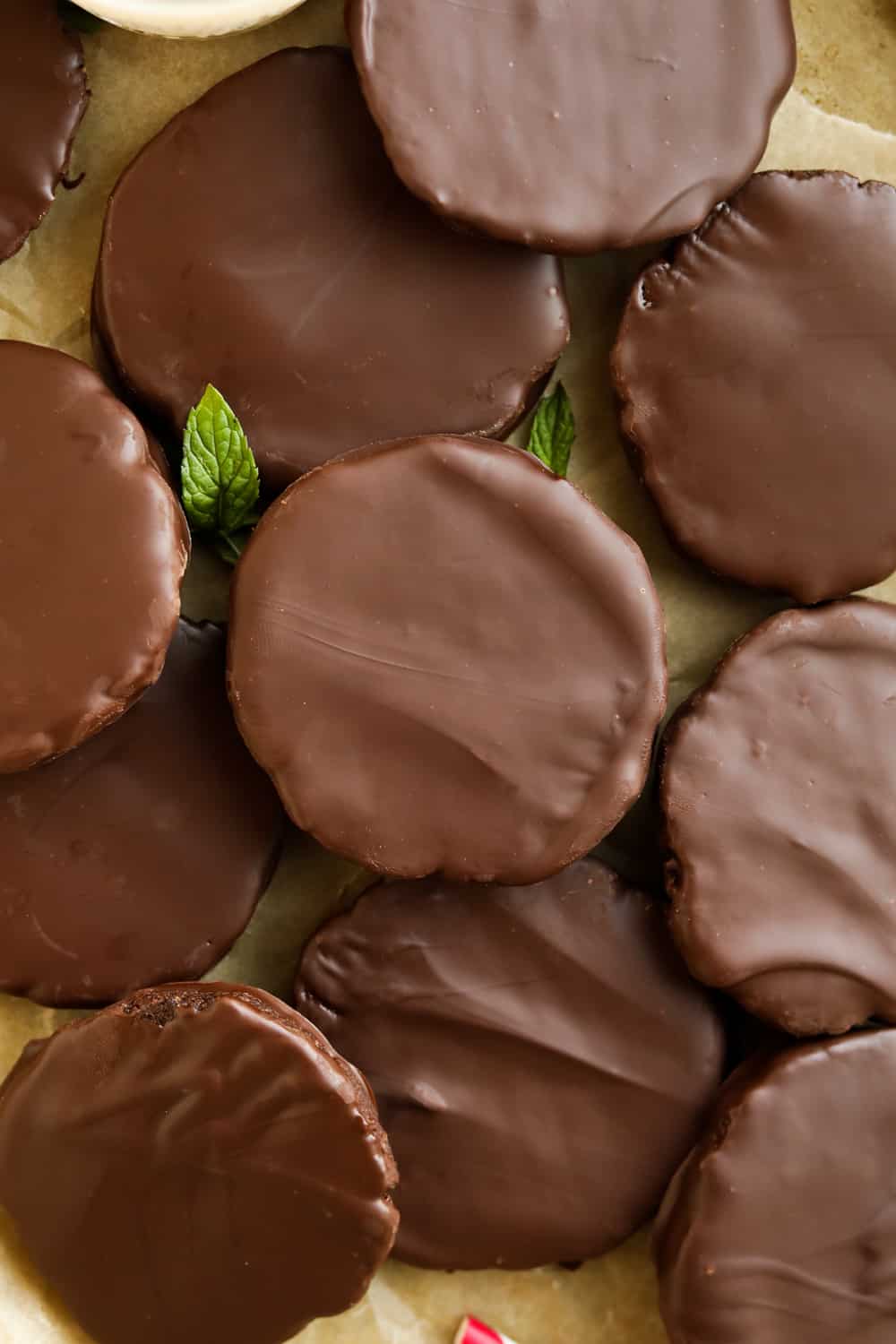 Chocolate covered cookies On a piece of brown parchment paper with mint leaves next to them.