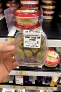 A hand holding a package of Greek olives.