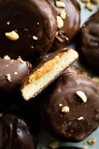 A chocolate cookie cut in half with peanut butter oozing out of it. The cookie is set on top of other cookies covered in chocolate.