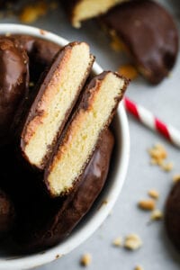 A cookie that has been covered in chocolate and cut in half, and is set inside a bowl of other chocolate covered cookies.