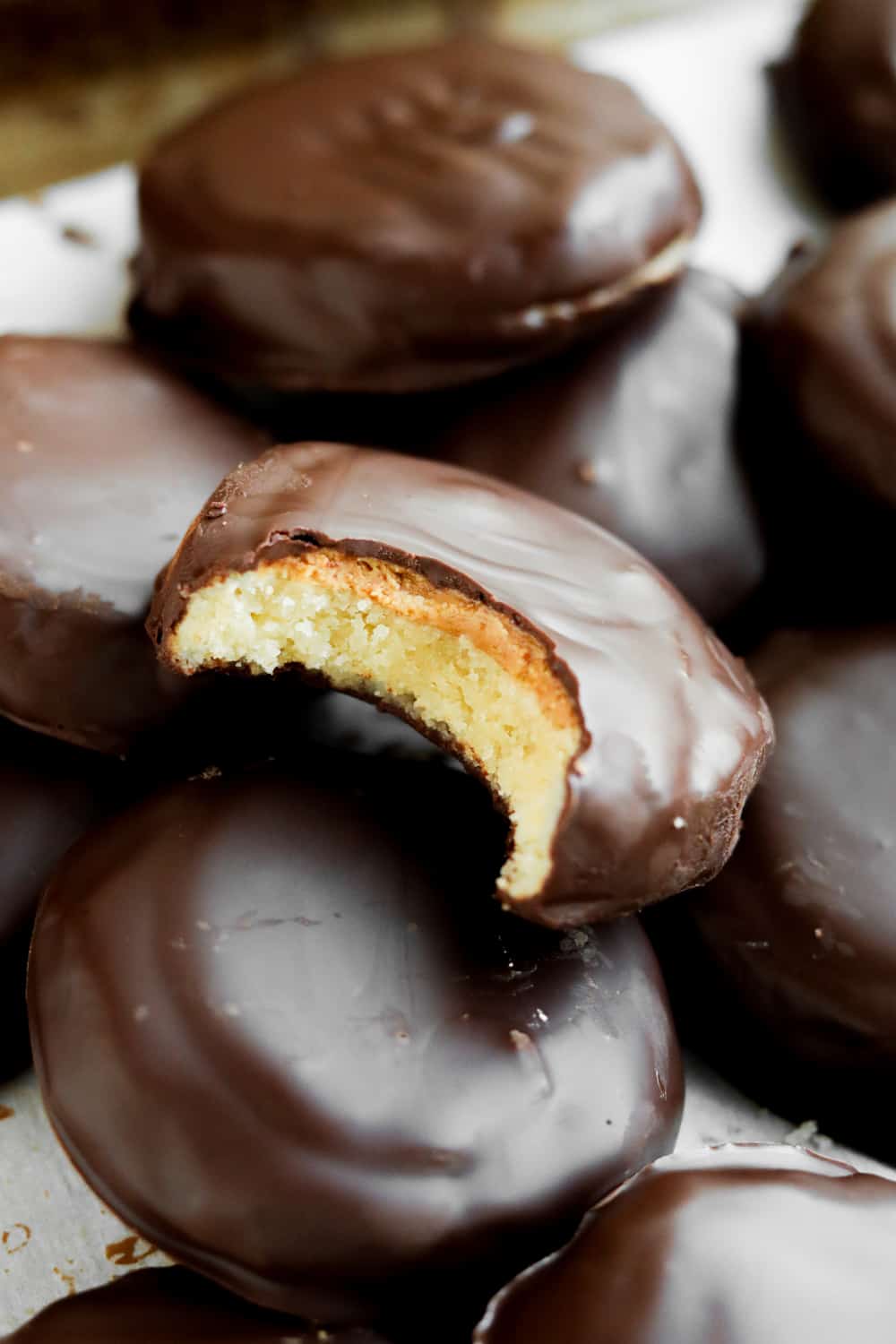 A chocolate covered cookie with a bite taken out of it that's set on top of other chocolate cookies.