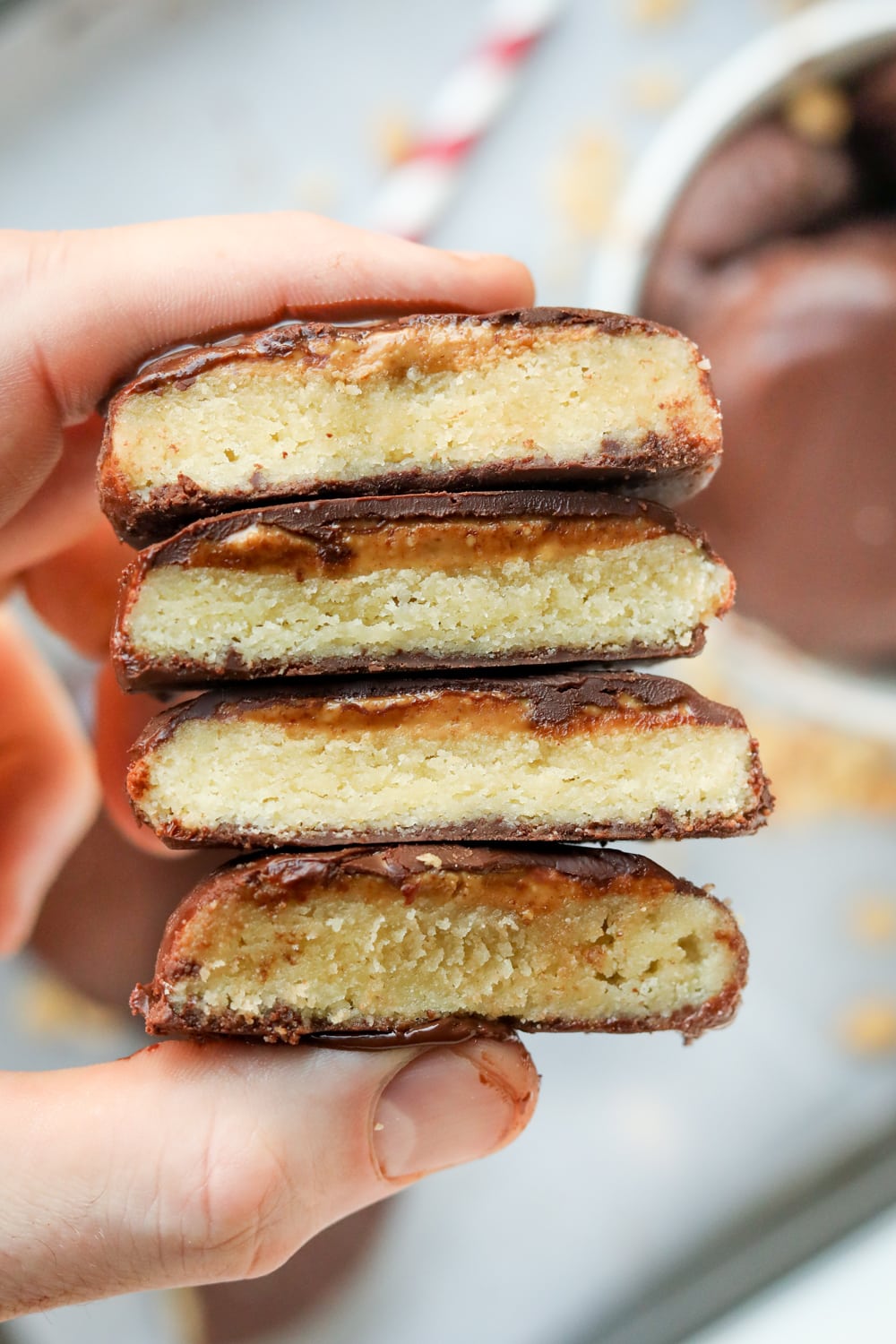 A hand holding a stack of chocolate covered cookies that have been cut in half.