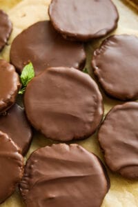 Chocolate coated cookies stacked on top of one another on a piece of brown parchment paper with a mint leaf next to them.