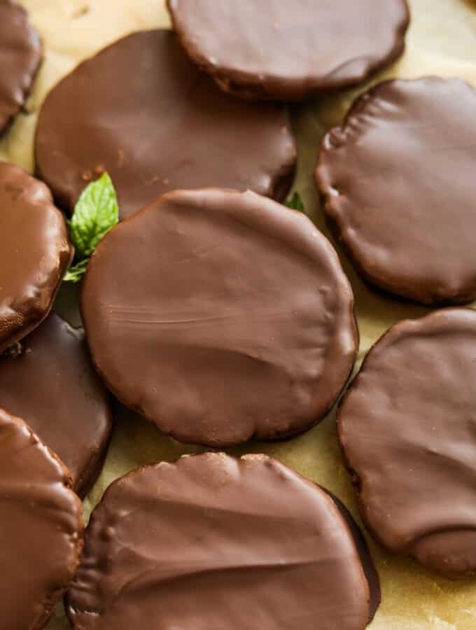 Chocolate coated cookies stacked on top of one another on a piece of brown parchment paper with a mint leaf next to them.