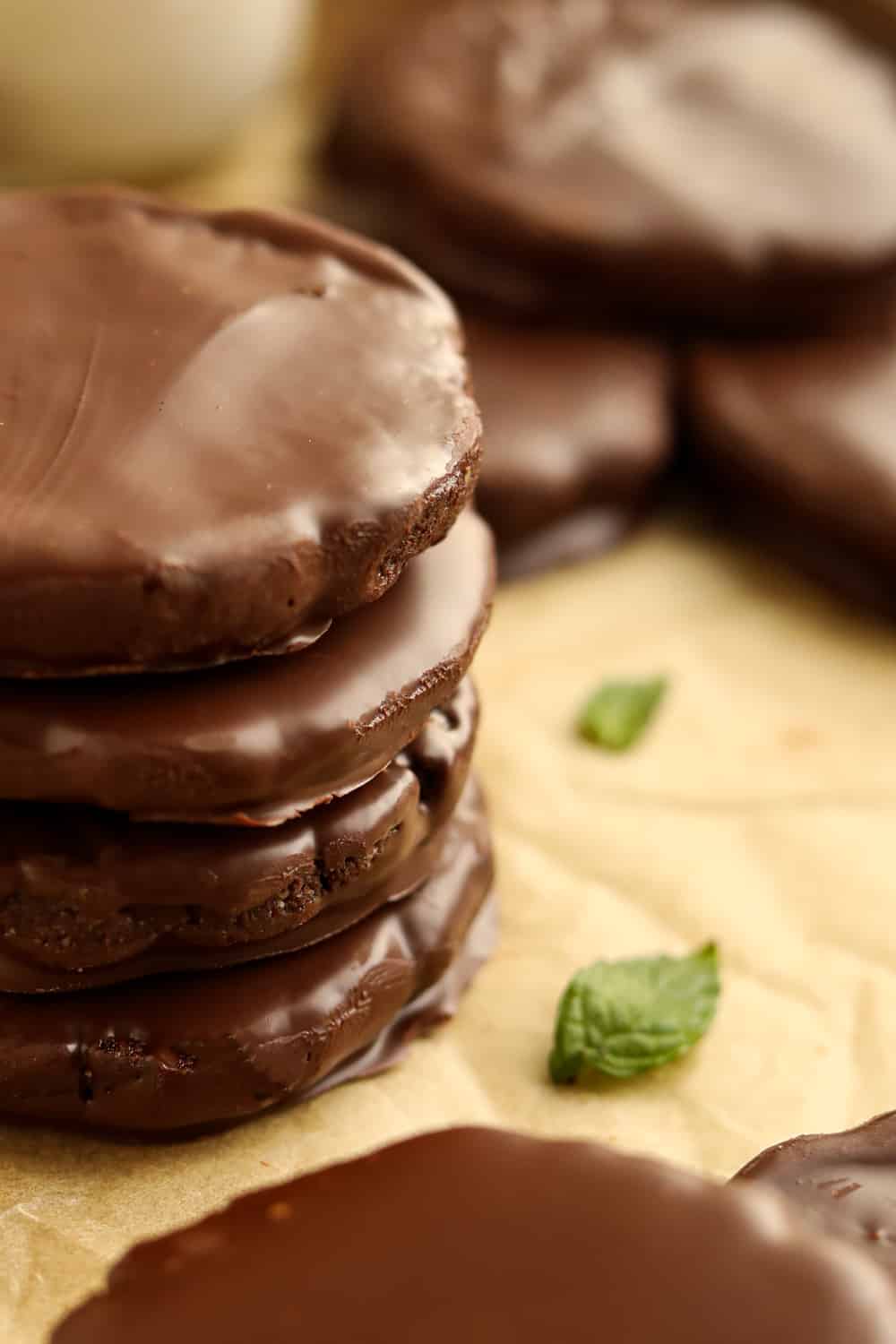 The side of four chocolate cookies stacked on top of each other; there are two green mint leaves next to the cookies.