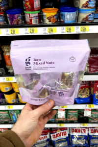 A hand holding a package of raw mixed nut snack packs.