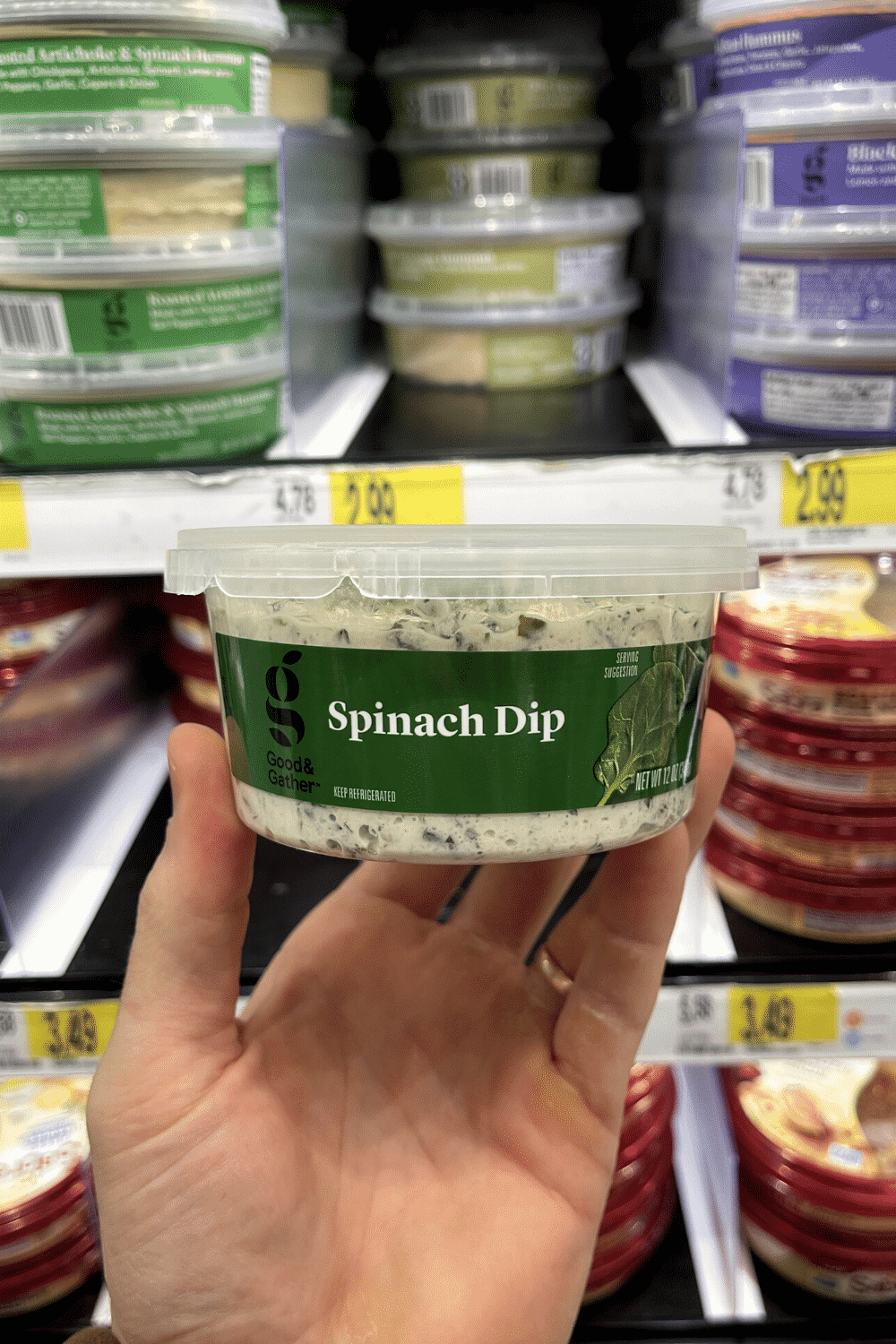 A hand holding a container of spinach dip.